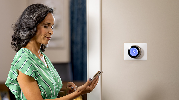 Woman looking at smartphone next to thermostat